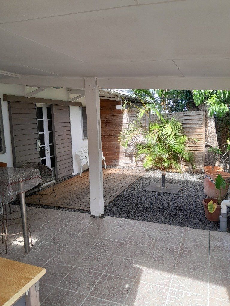 vue de l'entrée du T1 : cuisine à gauche, terrasse couverte avec porte d'entrée de la pièce principale (en blanc) et jardinet